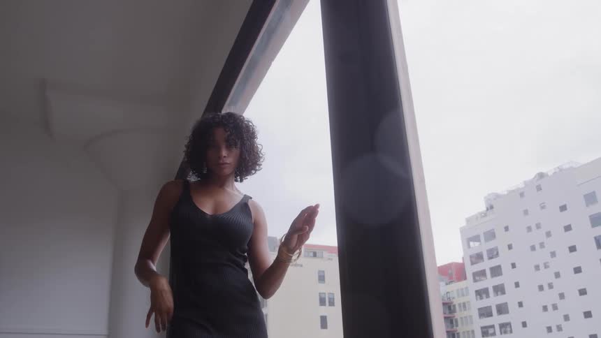 Woman standing in front of windows in her apartment with a view of towers and skyscrapers