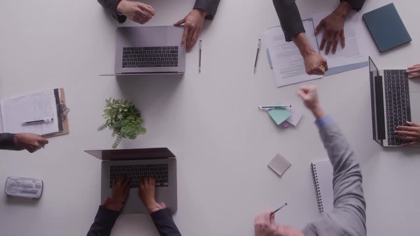 Professionals work at a table while two of them shake hands in the center