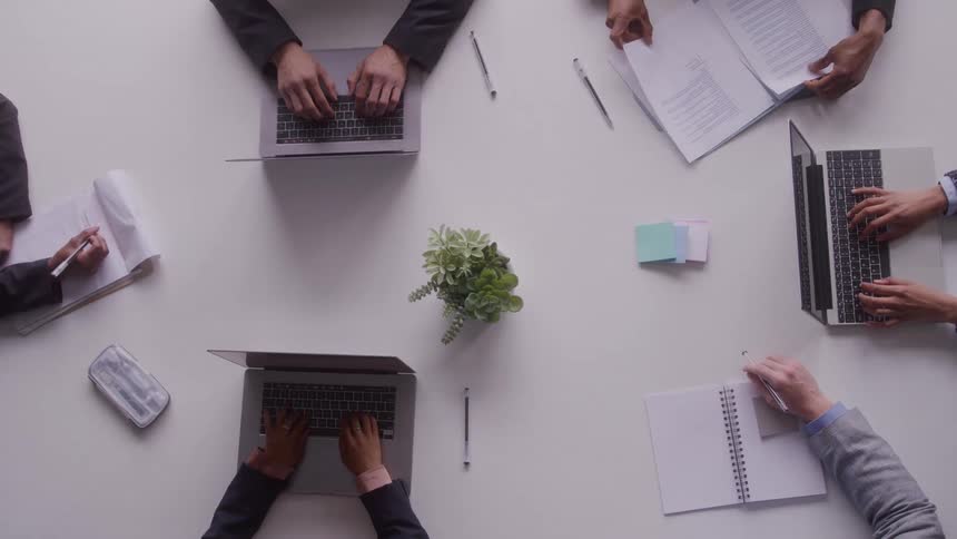 A group of colleagues collaborates around a conference table using laptops and reviewing documents