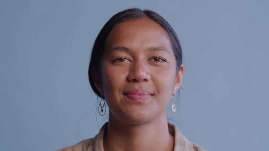 The woman is standing by a wall smiling