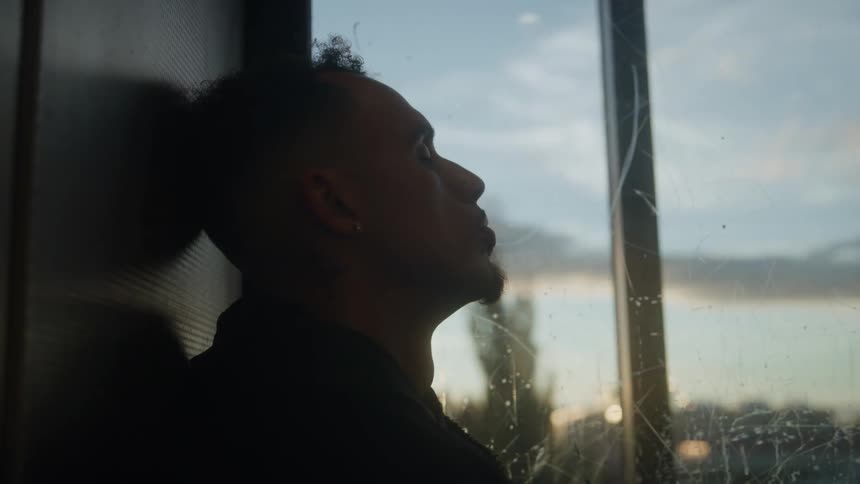 Man rests his head against the elevator wall while looking at the lateafternoon light through the window