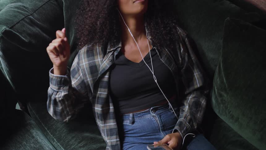 Woman sitting on the couch holding her music player and snapping her fingers to the sound