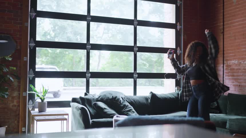 Girl dances in her living room while listening to music on earbuds attached to her smartphone