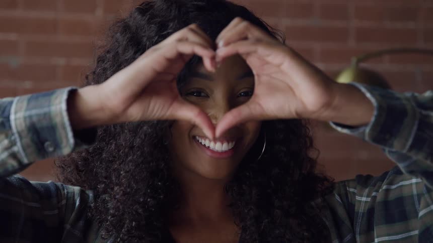 Woman smiles while forming a heart shape with her hands in front of her face