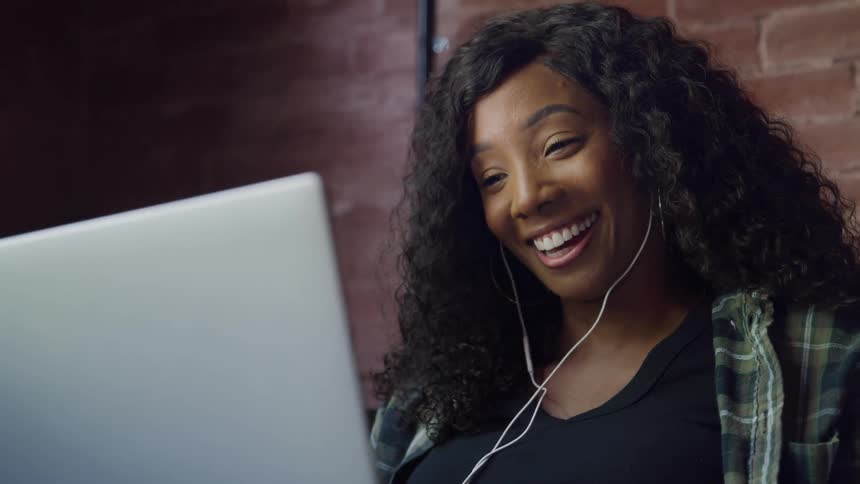 A woman waves and smiles at her laptop screen