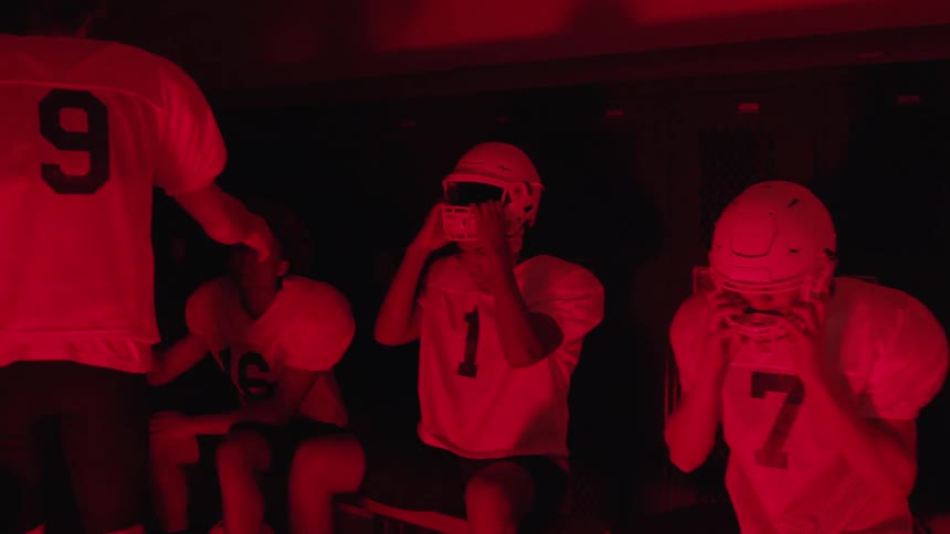 American football players get ready in a locker room lit by red light