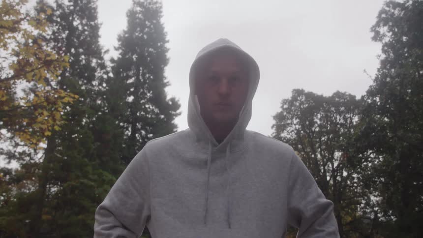 Man wearing a hooded sweatshirt stands outdoors among the trees