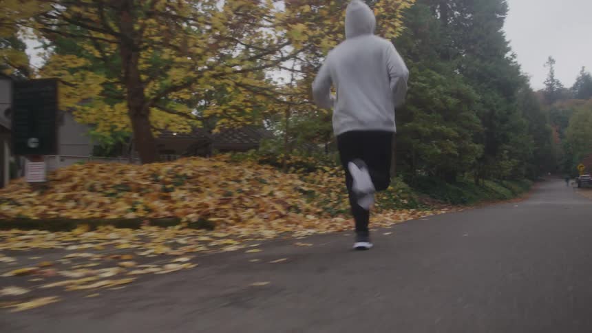 Man wearing a hoodie runs down a neighborhood street