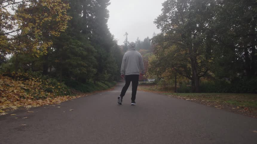 Man wearing a hoodie stands on a neighborhood street moving his arms and legs in exercise