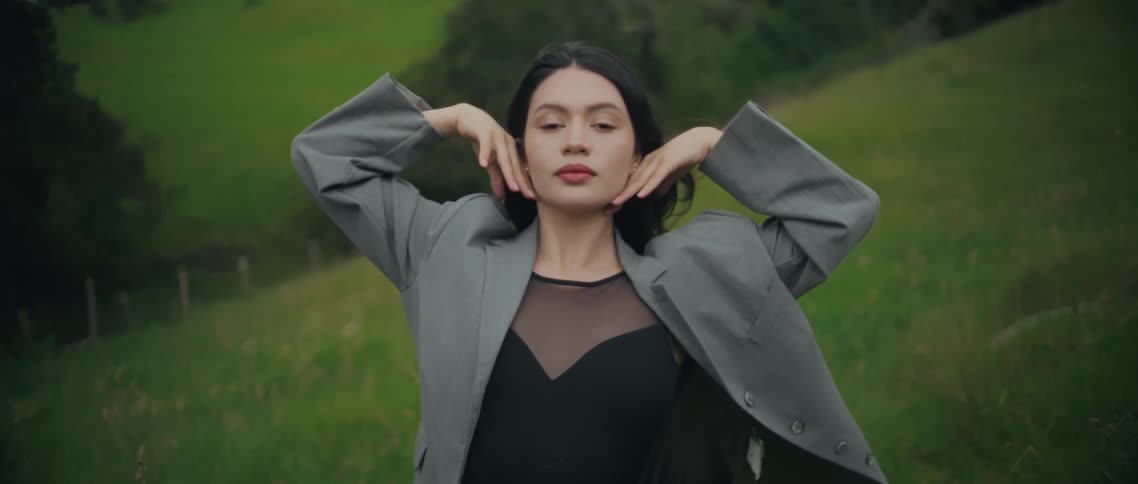 Woman places her hands beside her face while looking to the left in a green field