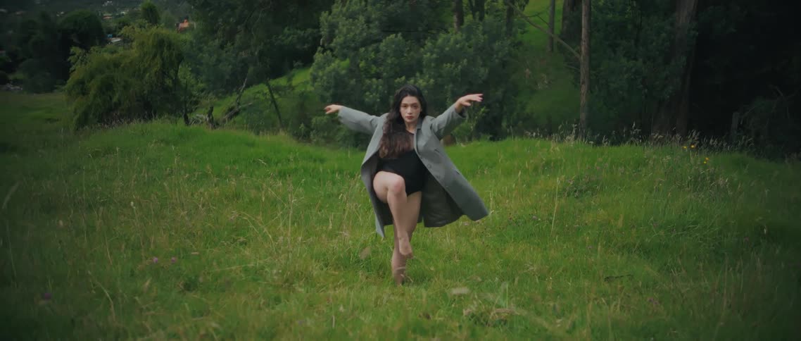 Woman performs a balancing pose with arms extended in the middle of a green field