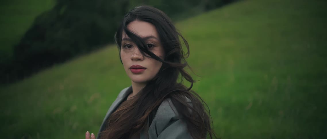 Woman standing on a grass covered hill as her hair moves in the breeze