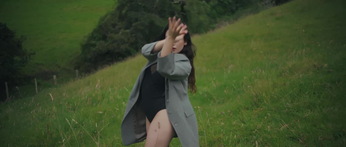 Woman raises her arms overhead while dancing on a green hillside