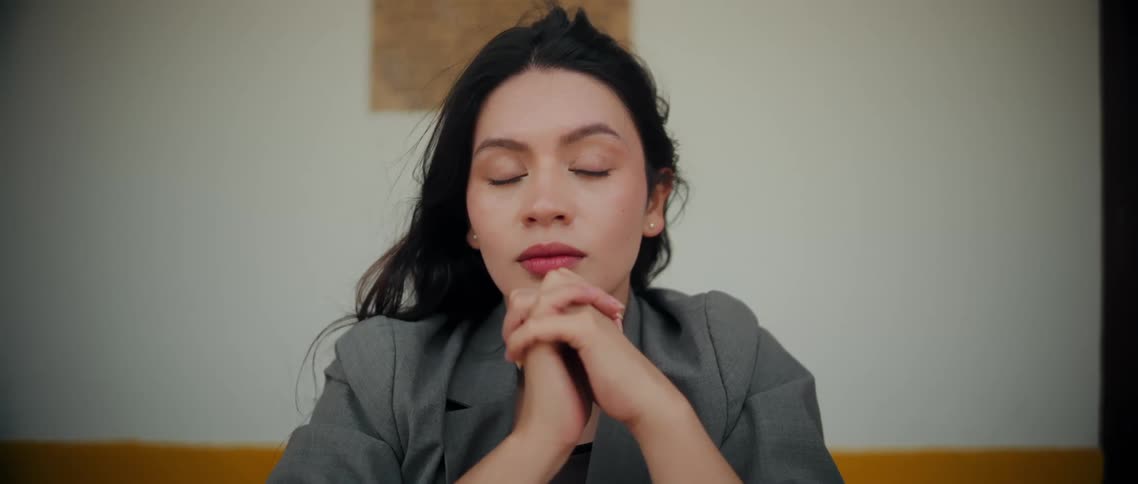 Woman rests her joined hands under her chin while holding a direct calm gaze