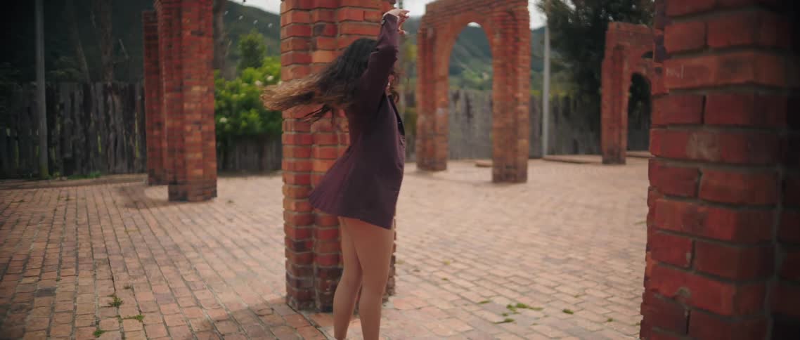 A woman performs slow salsa dance moves in an outdoor courtyard with brick archways