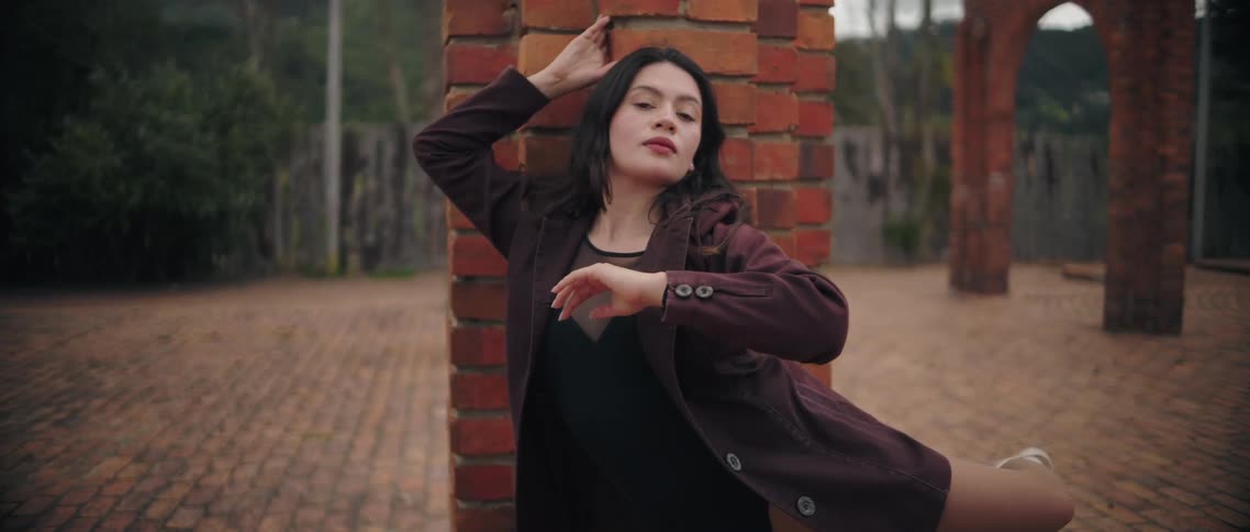 Woman rests one hand on the brick column while extending the other arm in an elegant pose