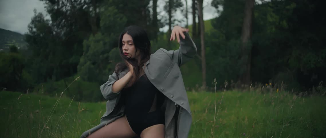 Woman standing in tall grass outside of the woods moving her arms with tai chi dance moves