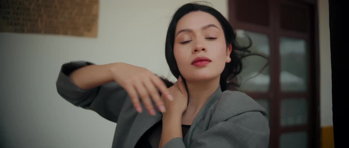 Woman raises her arm and touches her forehead while directing her gaze upward