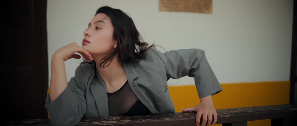 A woman in a grey blazer dances expressively against a wooden railing sweeping her hands through her hair and extending her arms in fluid graceful motions