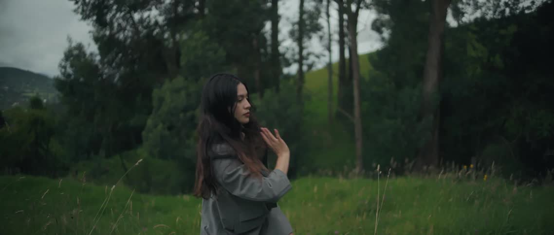 A woman performs slow expressive dance movements in a grassy outdoor field