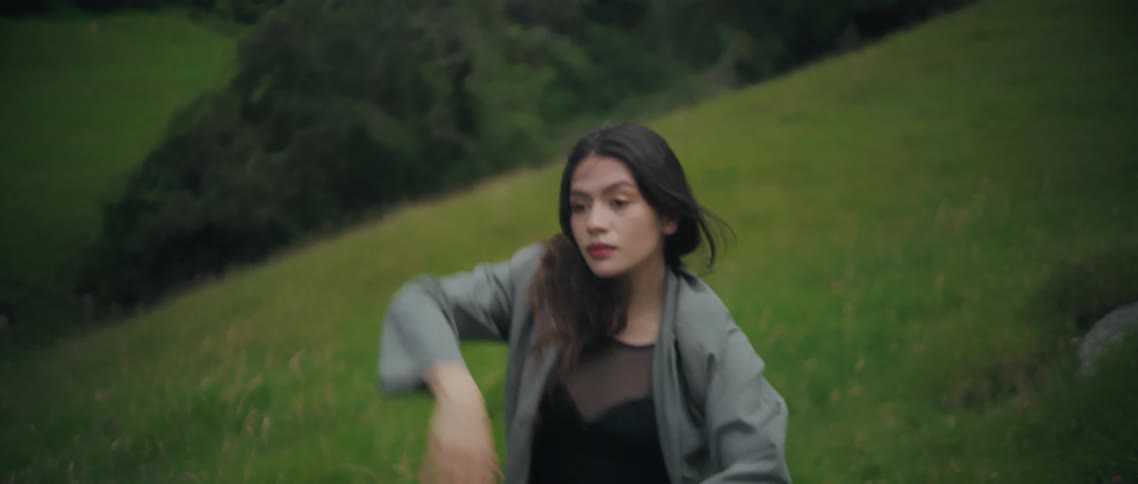 A young woman dances while standing on a hillside on a summer day