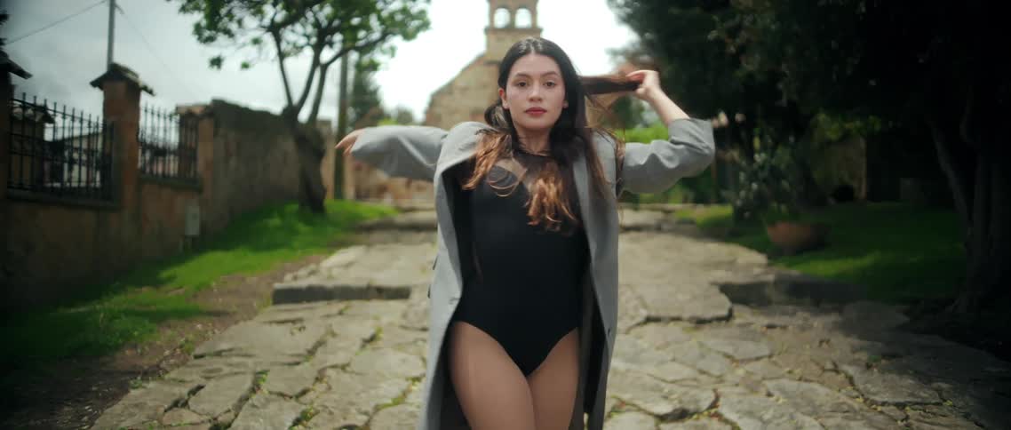 A woman performs slow graceful dance movements along a stone path in an outdoor garden