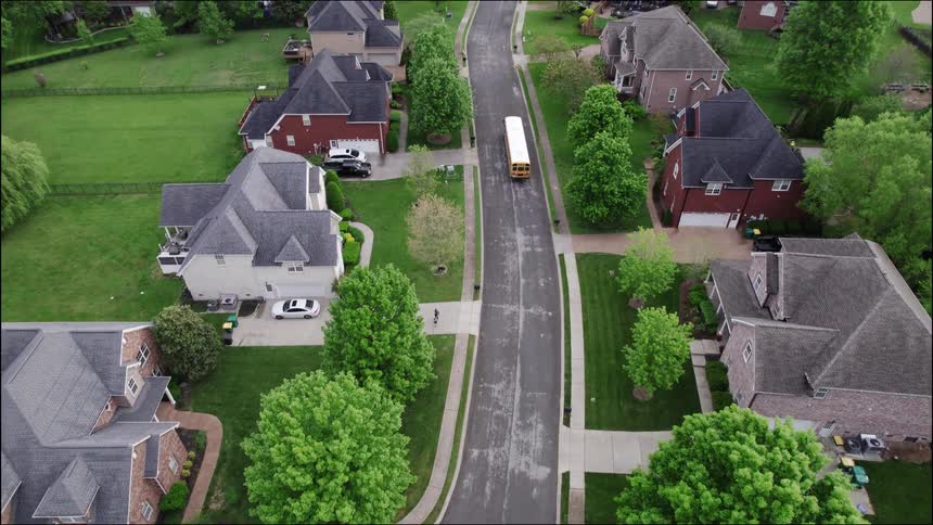 School bus moves along the street passing through a residential neighborhood on a summer day