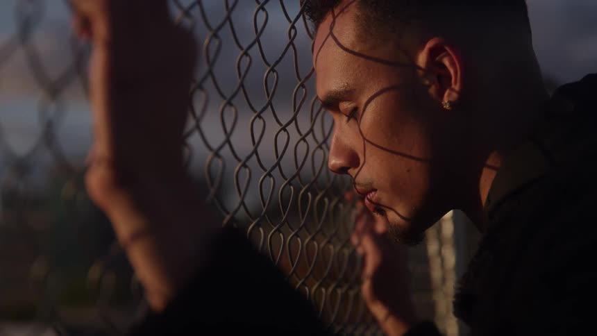 Man leaning against the fence with eyes closed in the sunset light