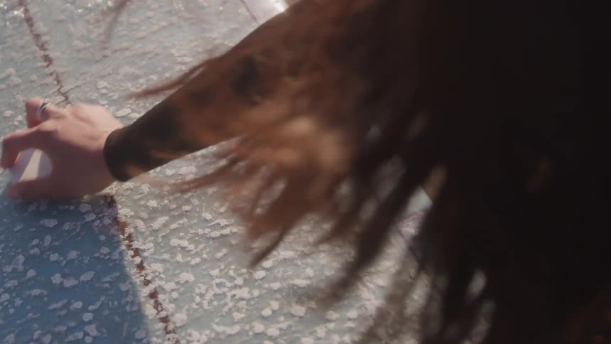The woman is polishing a snowboard on the sand