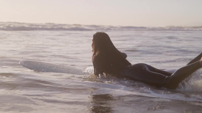 Surfer lying on the board gliding through shallow water at sunrise