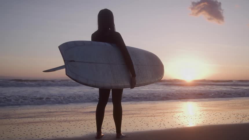 The surfer watches the sunrise on the beach