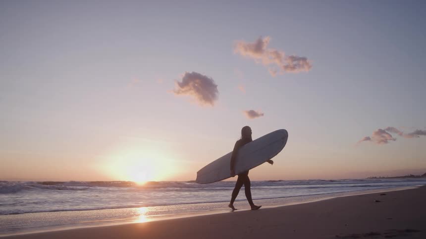 A person carrying a surfboard on the beach at dusk