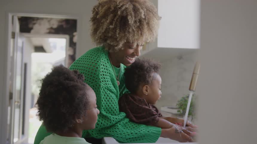 Mother helping the children wash their hands at the kitchen sink
