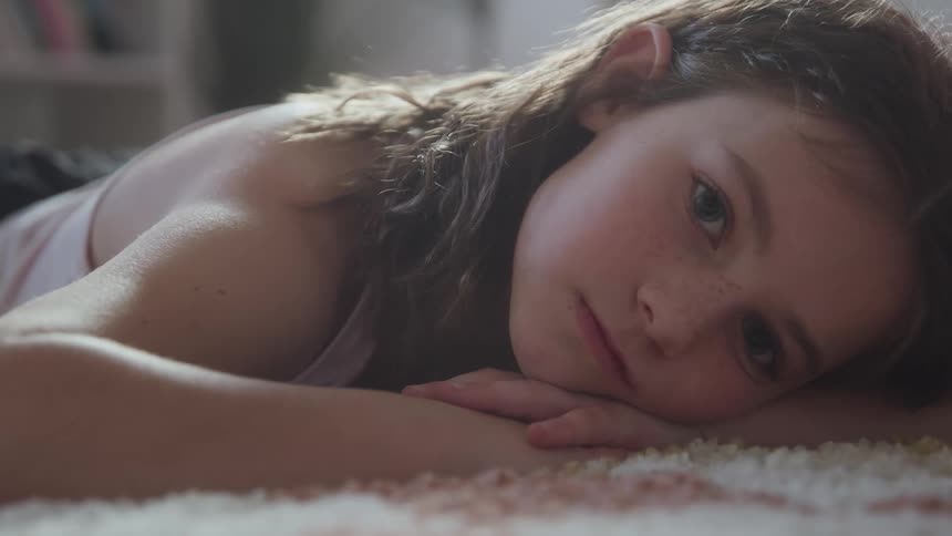 Little girl lying on carpeted floor with head resting on arms