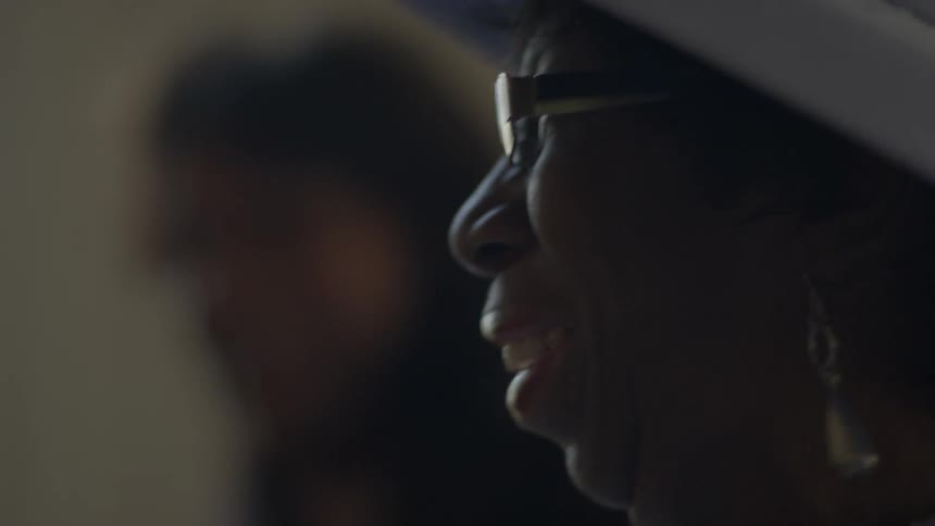 Older woman wearing white hat smiling and singing and dancing