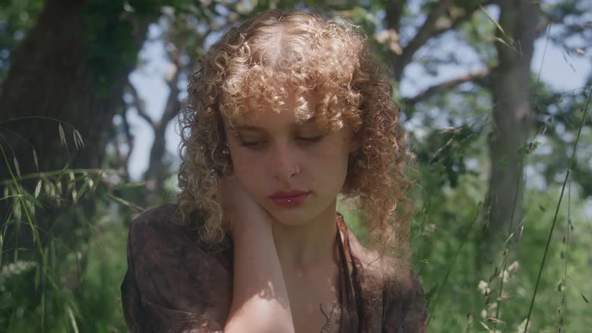Young woman sitting in the grass looking down among trees