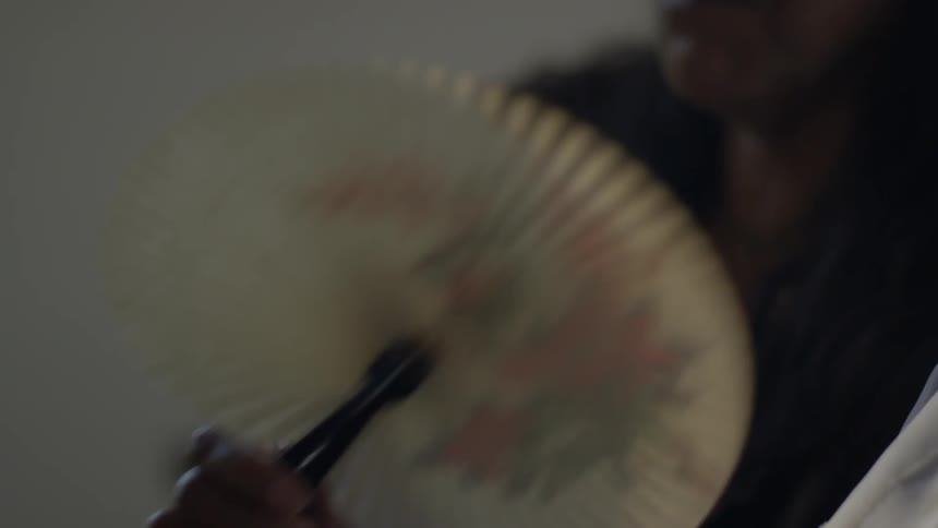 A woman fans herself with a paper fan