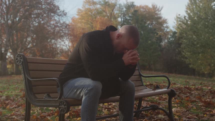 Man sitting on the bench with his head down among autumn leaves