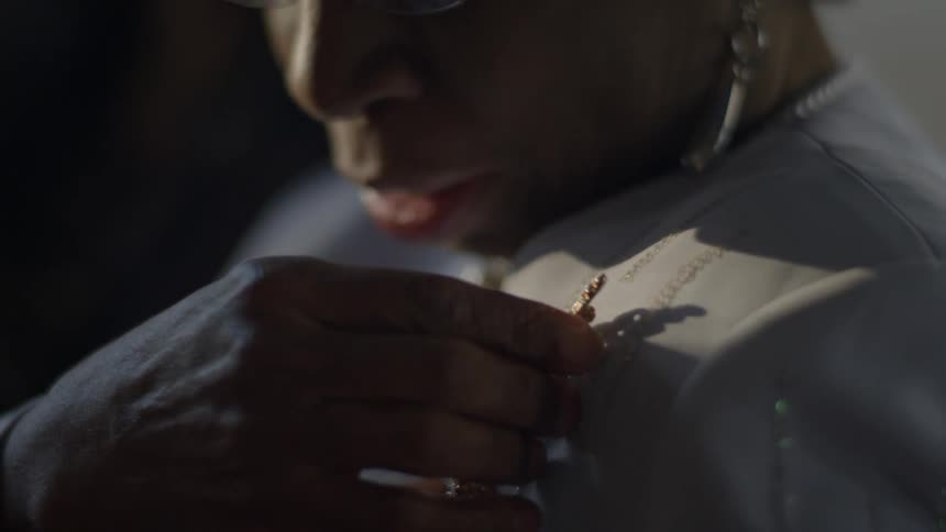 A man with glasses touching a pendant on his shirt