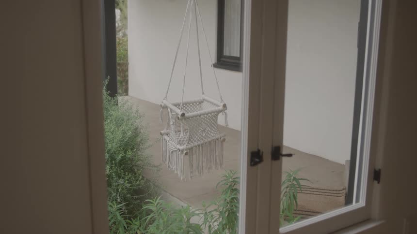 Macram swing chair hanging on the porch seen through the doorway