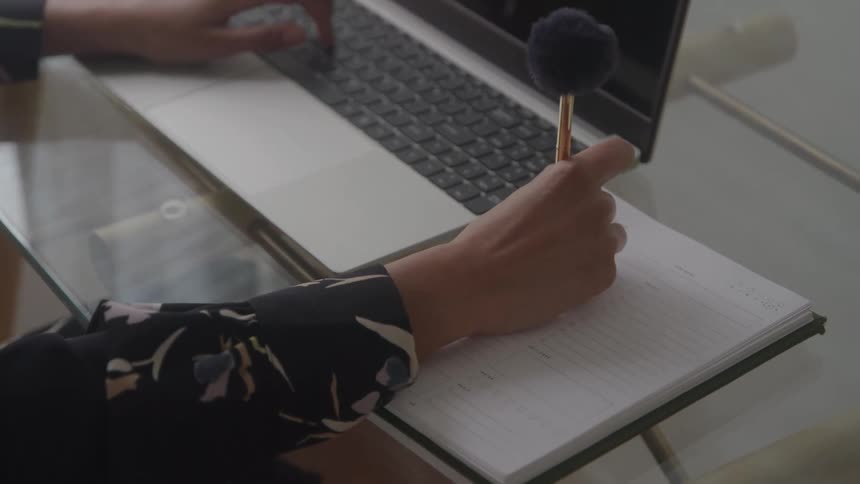 Woman sitting in front of a laptop makes a note in a notebook