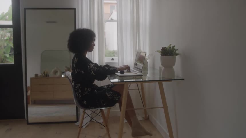 Woman working on a laptop while seated at a desk near the window