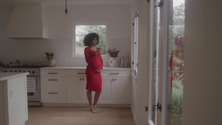 Pregnant woman in red dress drinking water in a modern kitchen