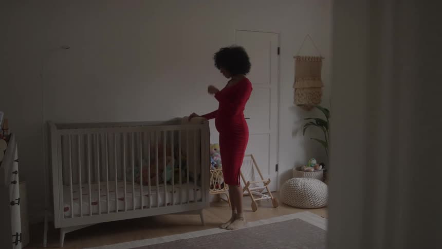 Pregnant woman standing next to a baby crib as she rubs her belly