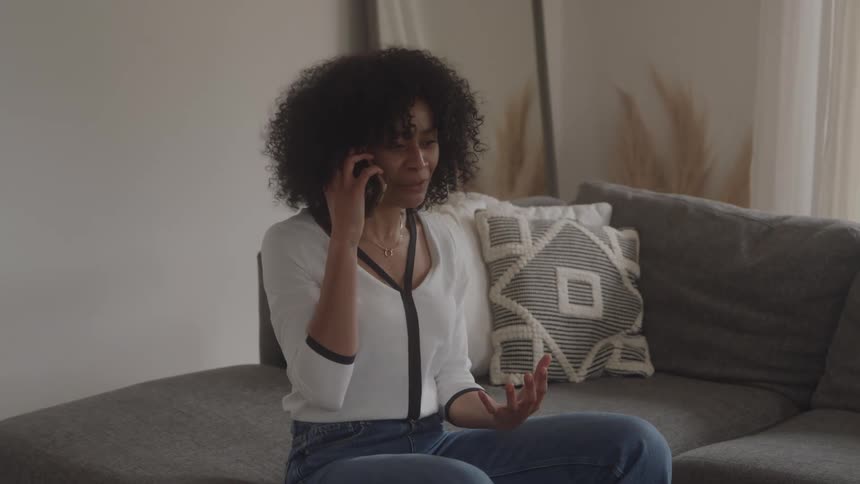 Woman sitting on the couch talking on the phone with an emotional expression