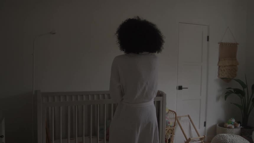 Mother holding the baby in the room lit by the window and placing him in the crib
