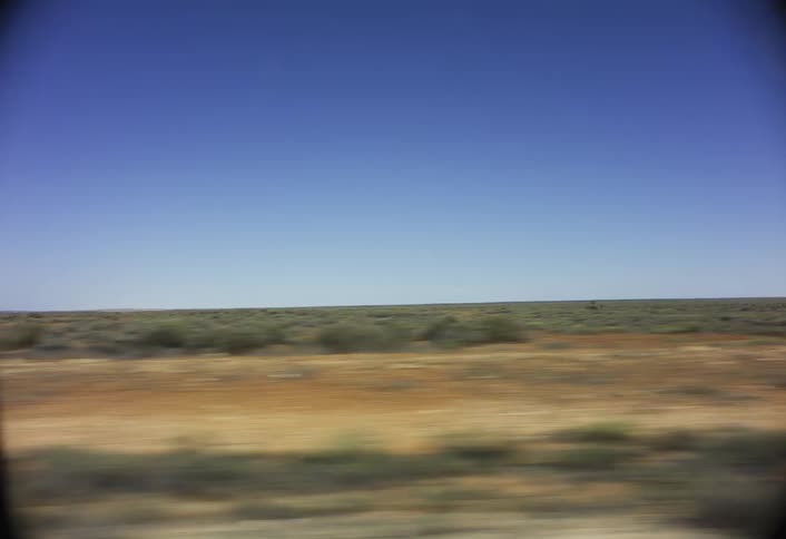 A blurry arid landscape speeds past the viewer under a vast clear blue sky capturing a sense of fast motion through the desert