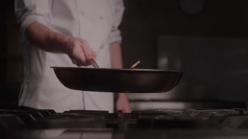 Close up of a male chef sauteing food in a pan over a cooker in a kitchen during daytime