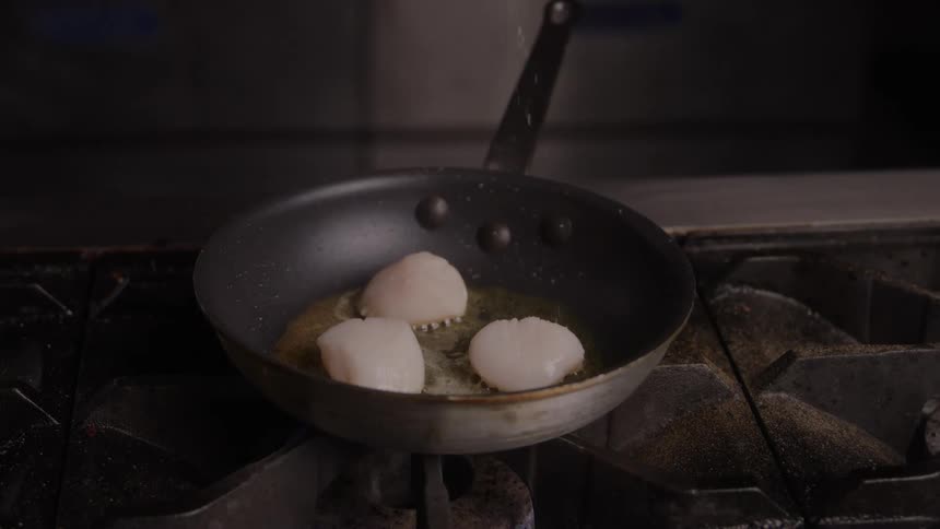 Salt being sprinkled over scallops as they cook in the pan