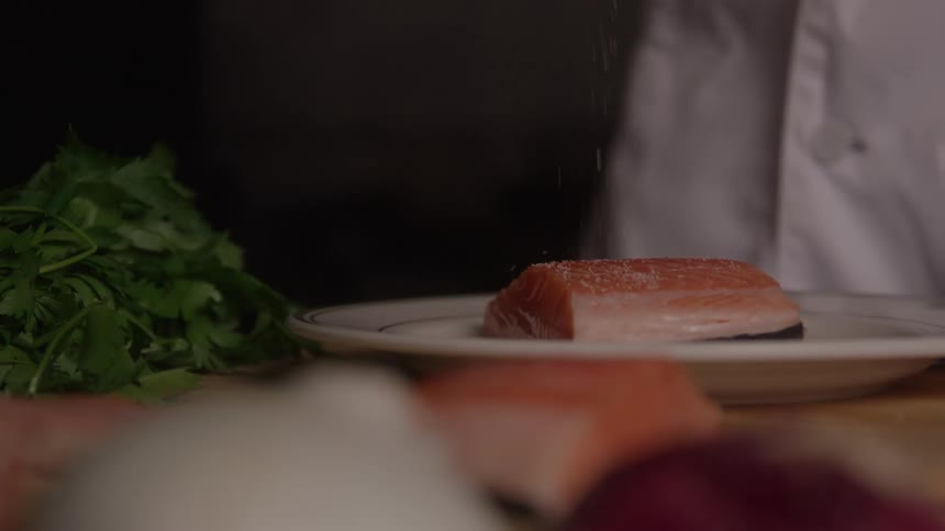 Salmon fillet being seasoned while resting on the plate